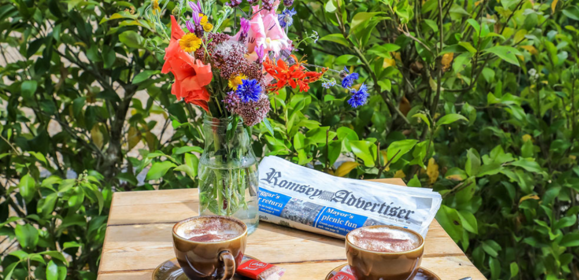 Vase of flowers, newspaper and two cups of coffee on an outside table
